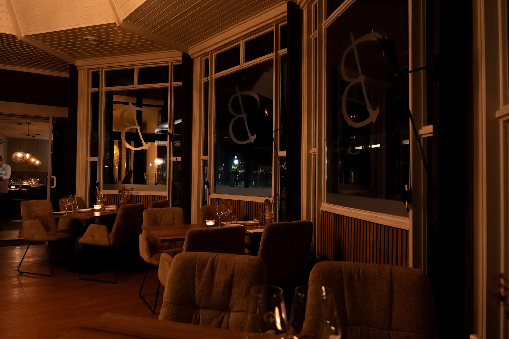 Serre met hoge ramen, gestileerde letters op het glas en fauteuils bij kaarslicht