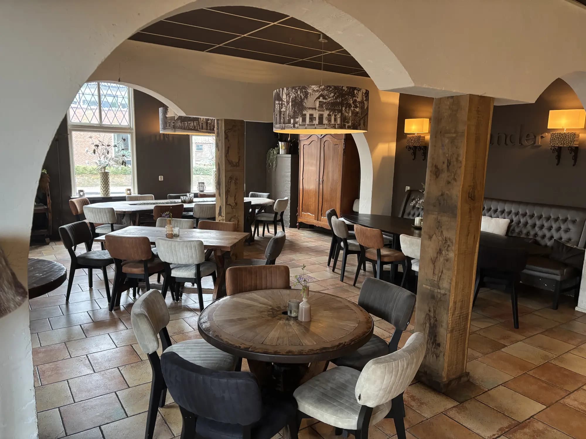 Eetzaal met witte gewelfbogen, houten tafels en terracotta vloer bij daglicht
