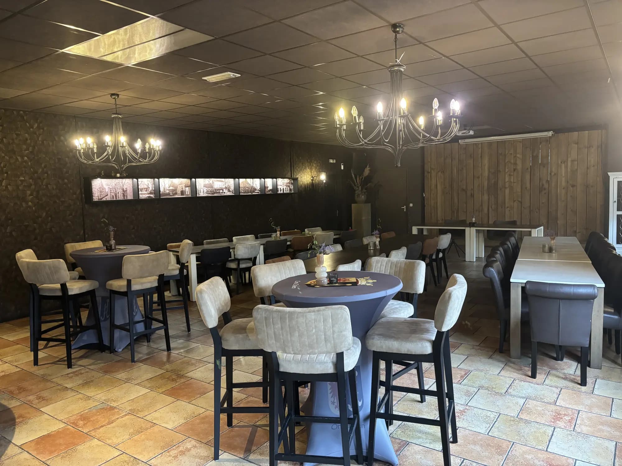 Zaal met statafels, barkrukken en kroonluchters, ingericht voor een borrel of feest