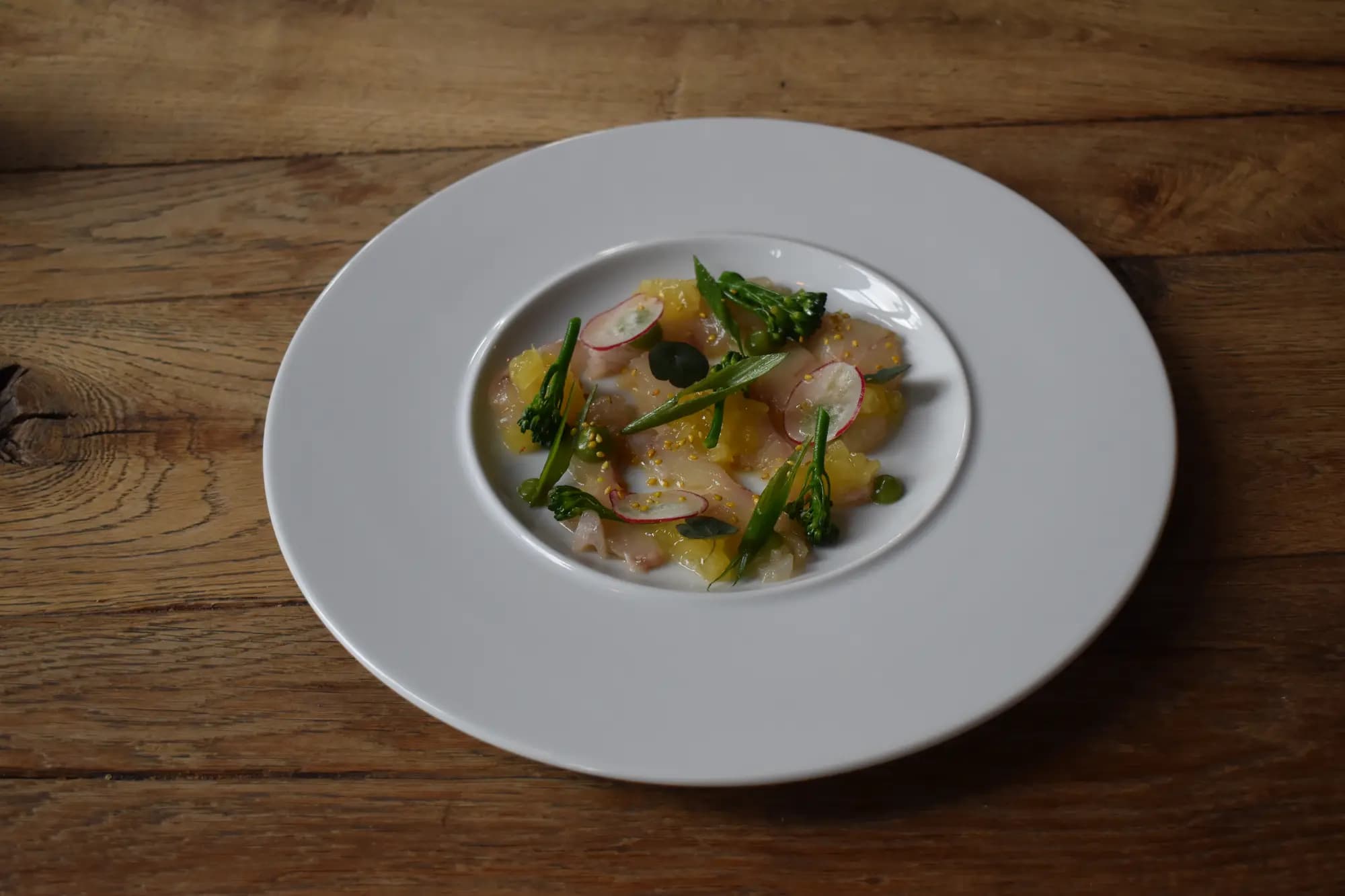 Voorgerecht van dungesneden witvis met citrus, radijs en kruiden op een diep wit bord