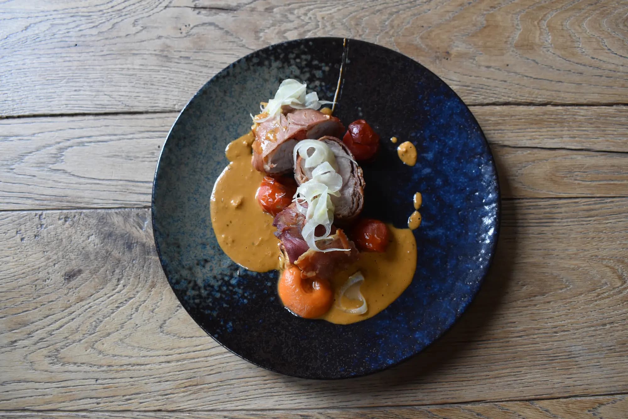 Rosé gebakken vlees met gepofte tomaatjes, venkel en romige saus op een blauw bord