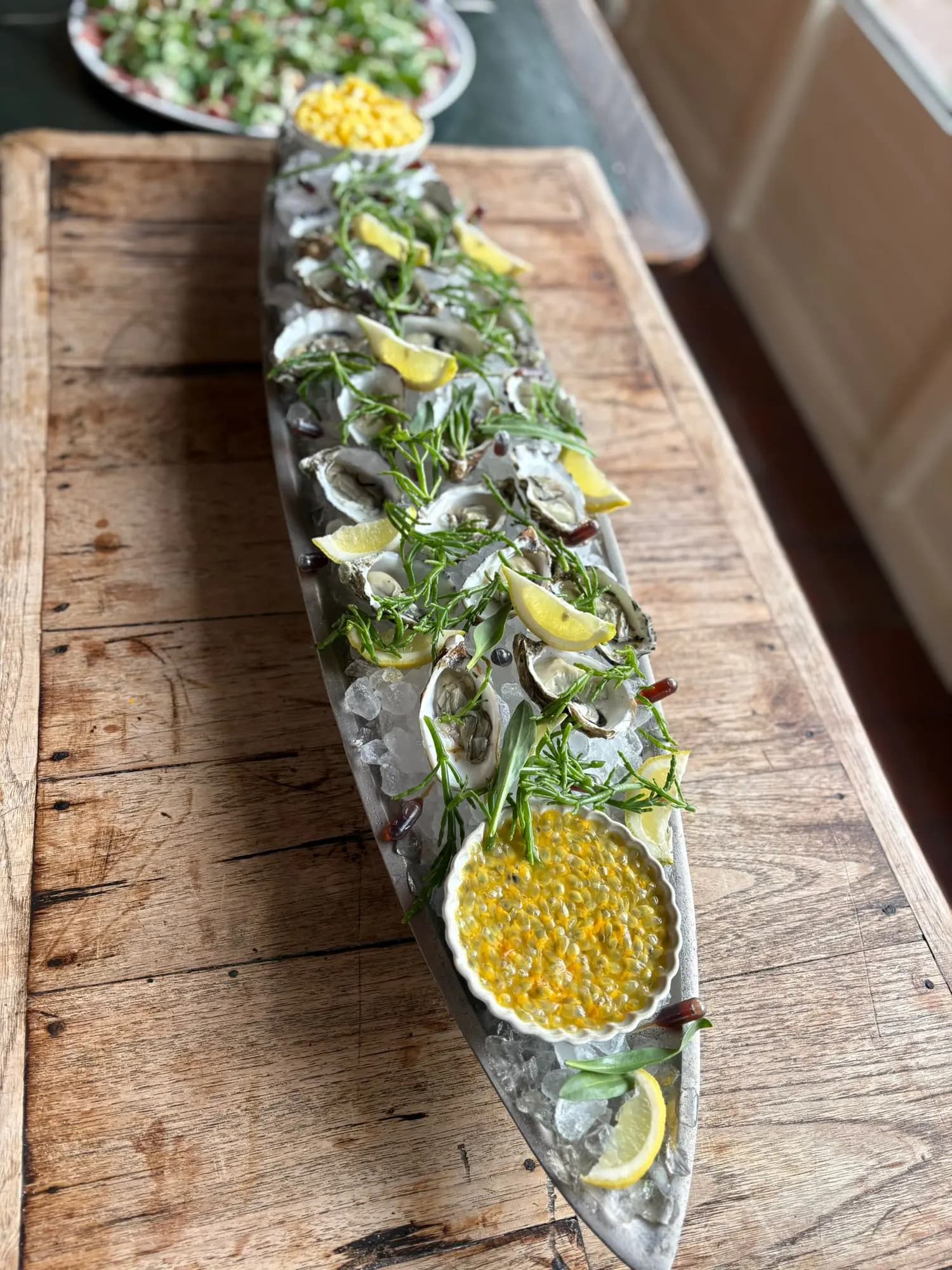 Langwerpige schaal met oesters op ijs, citroen, dille en een kom passievruchtdressing