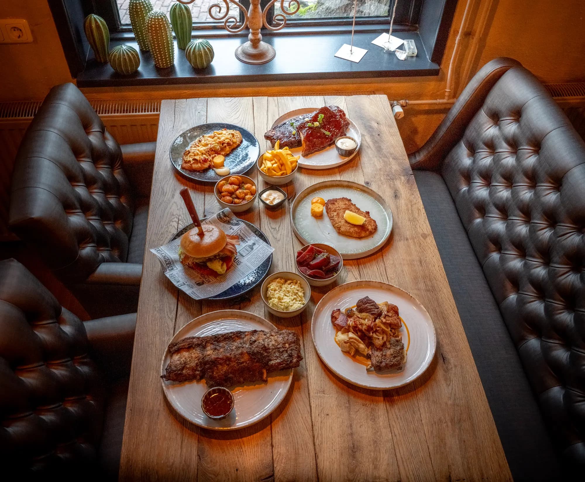 Bovenaanzicht van een tafel vol gerechten: spareribs, burger, schnitzel, friet en sausjes