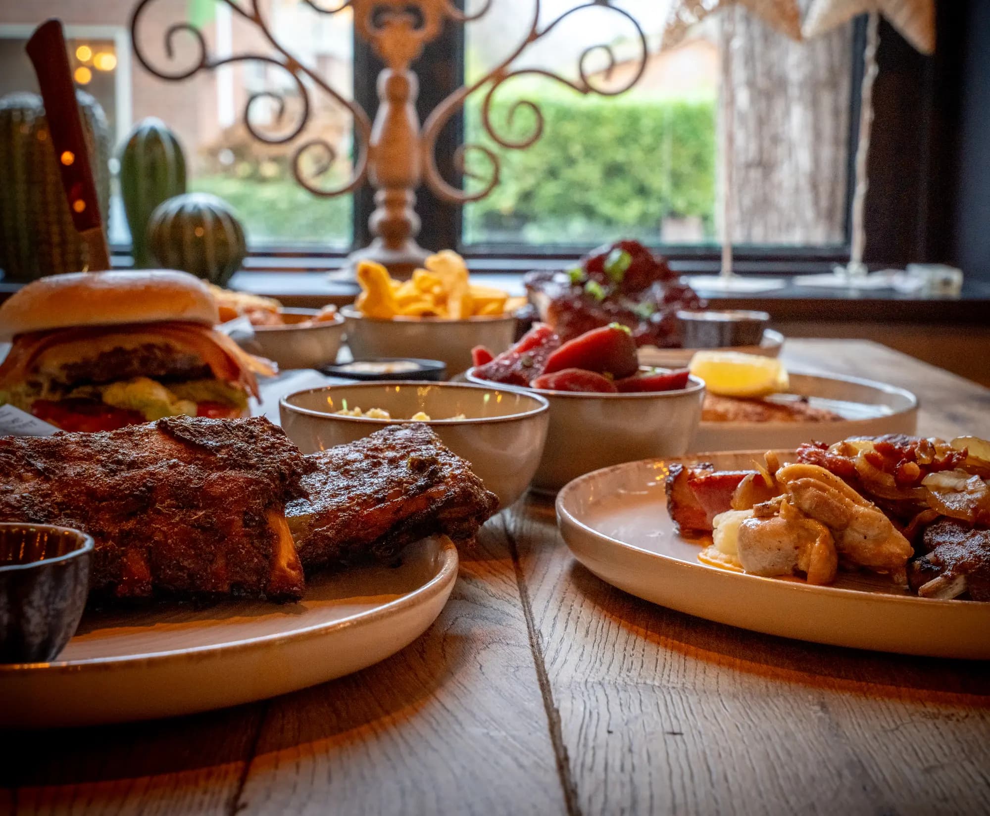 Close-up van spareribs met kruidenkorst, met burger, friet en sausjes op de achtergrond