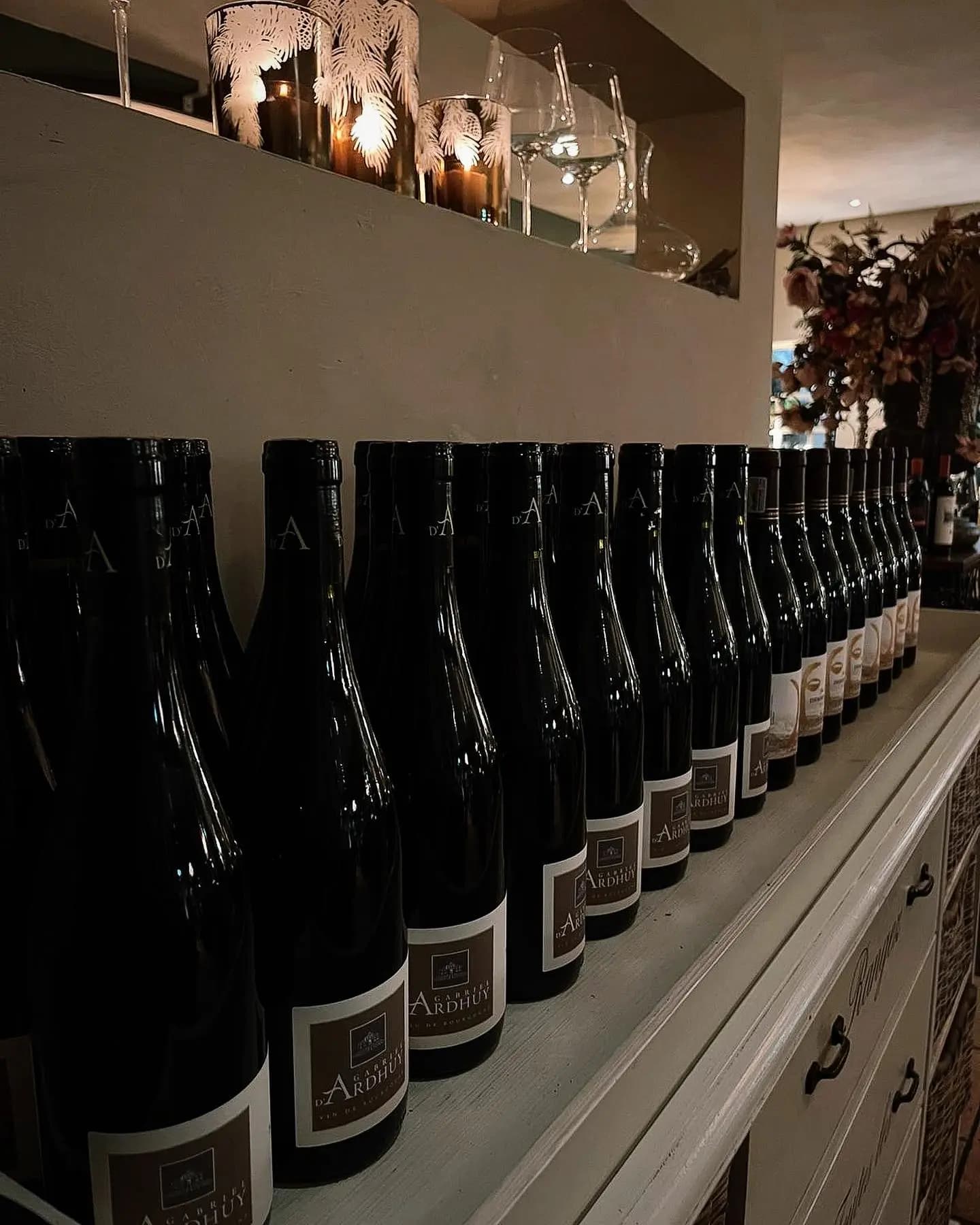 Rij wijnflessen op een richel met kaarsen en een wijnglas erboven in het restaurant