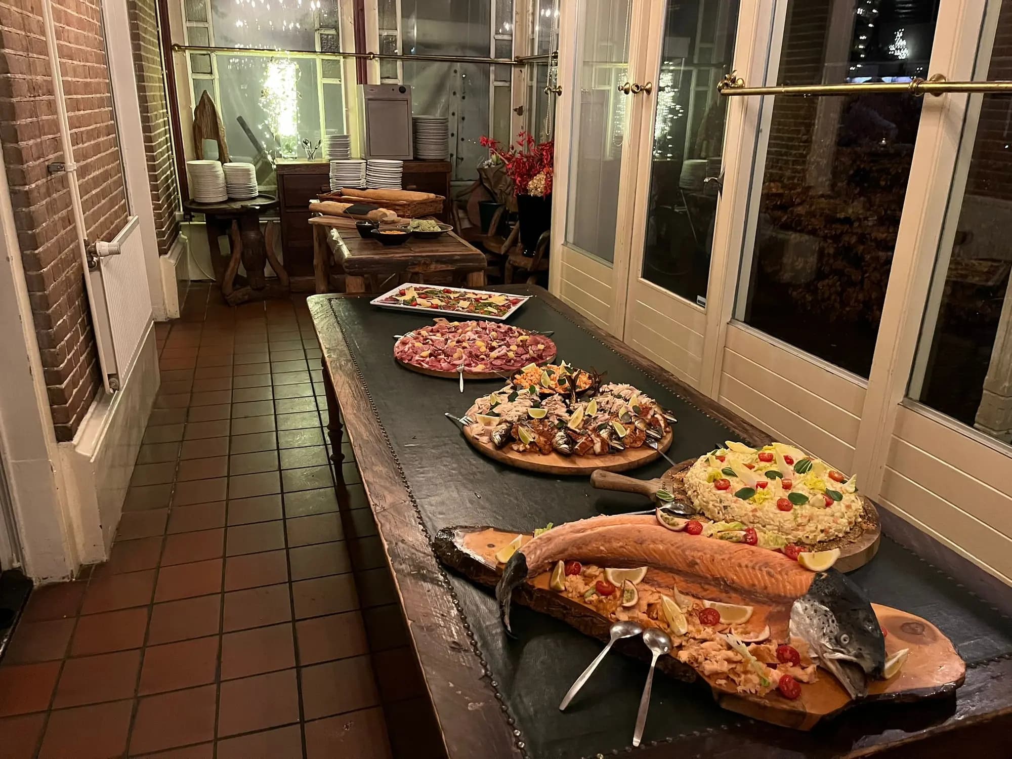 Koud buffet met hele zalm, salades en pizza's op een lange houten tafel in een serre