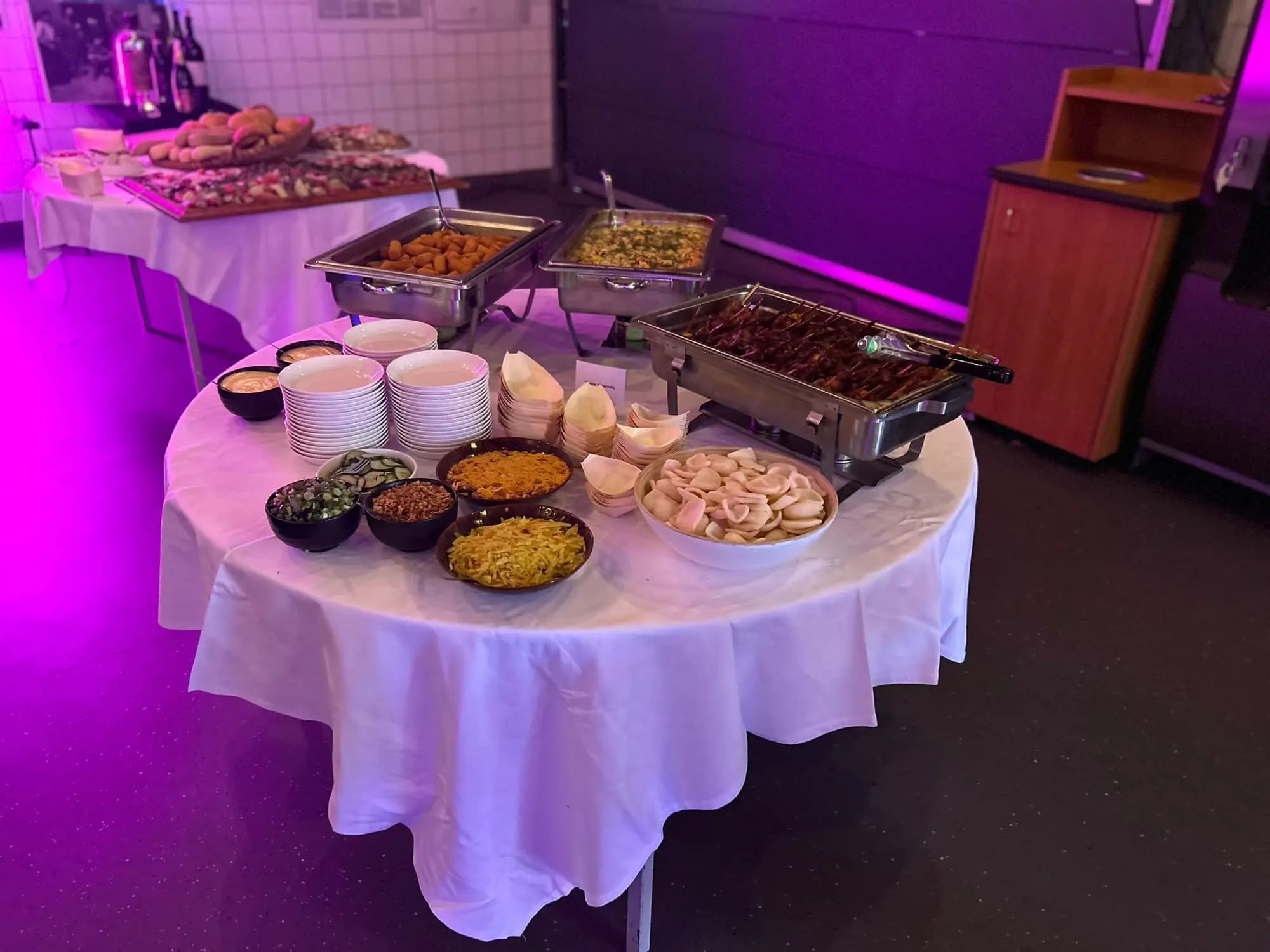 Buffet met chafing dishes, salades en bijgerechten in een feestzaal met paarse sfeerverlichting