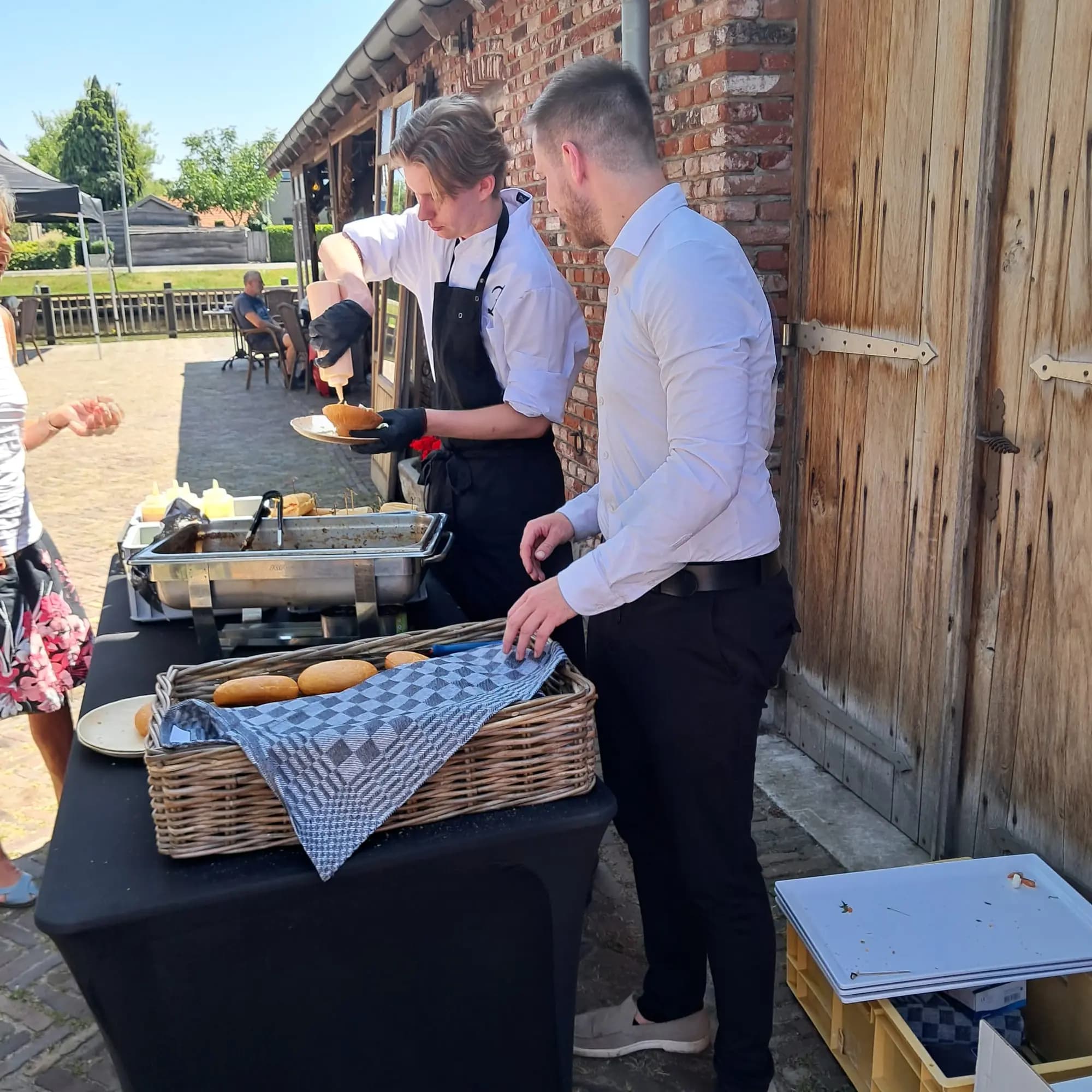 Kok schept een warm gerecht op het bord van een gast bij een buitenbuffet