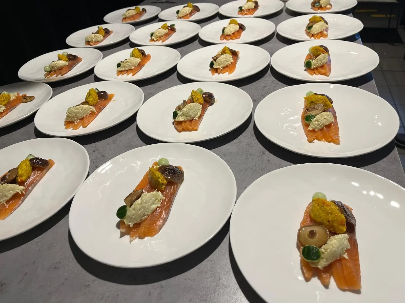 Gerookte zalm met crème en garnituur, klaargezet op een rij witte borden