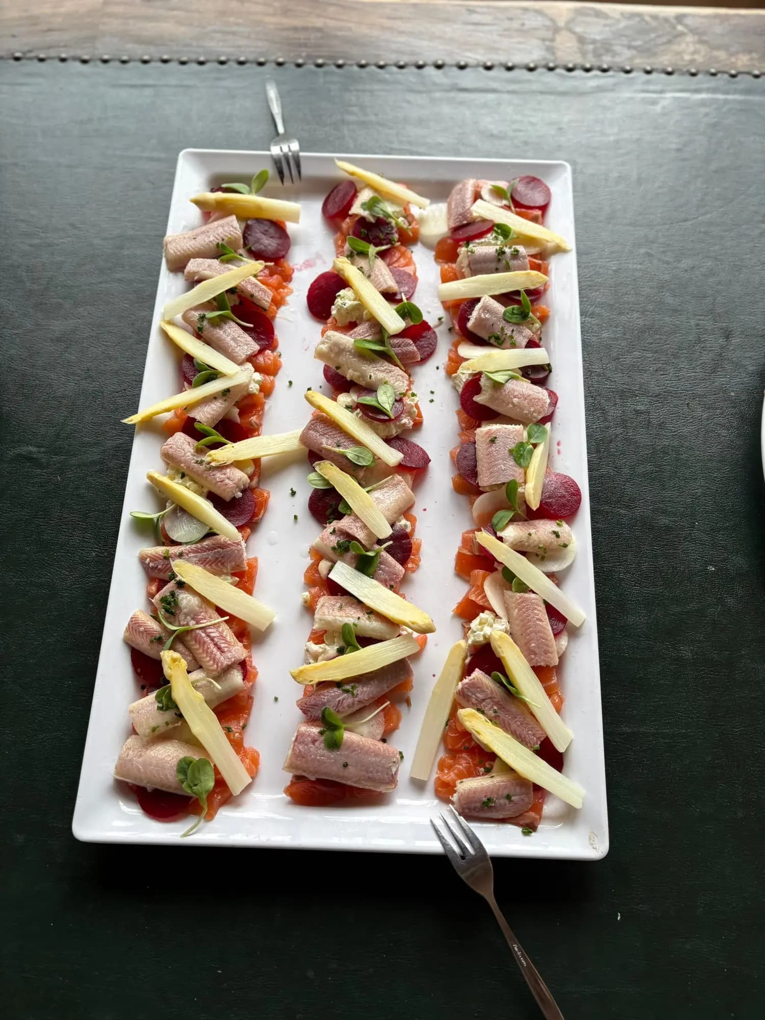 Visrolletjes met gerookte zalm, rode biet en witte asperge op een langwerpige schaal