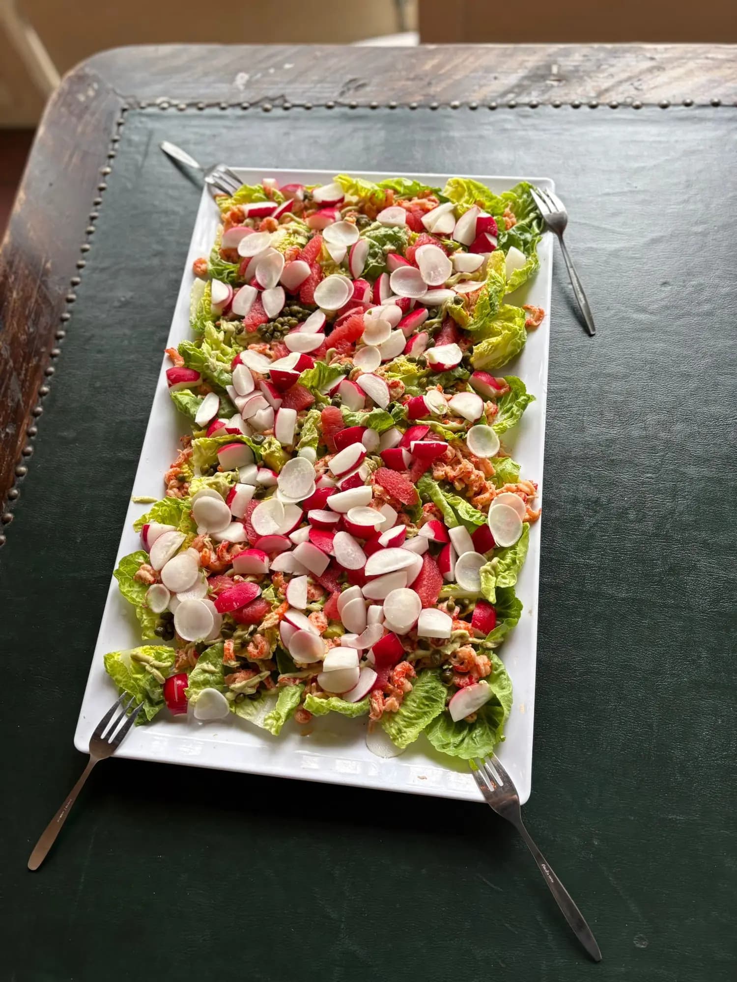 Salade met radijs, zalm en romaine op een rechthoekige schaal met serveervorken