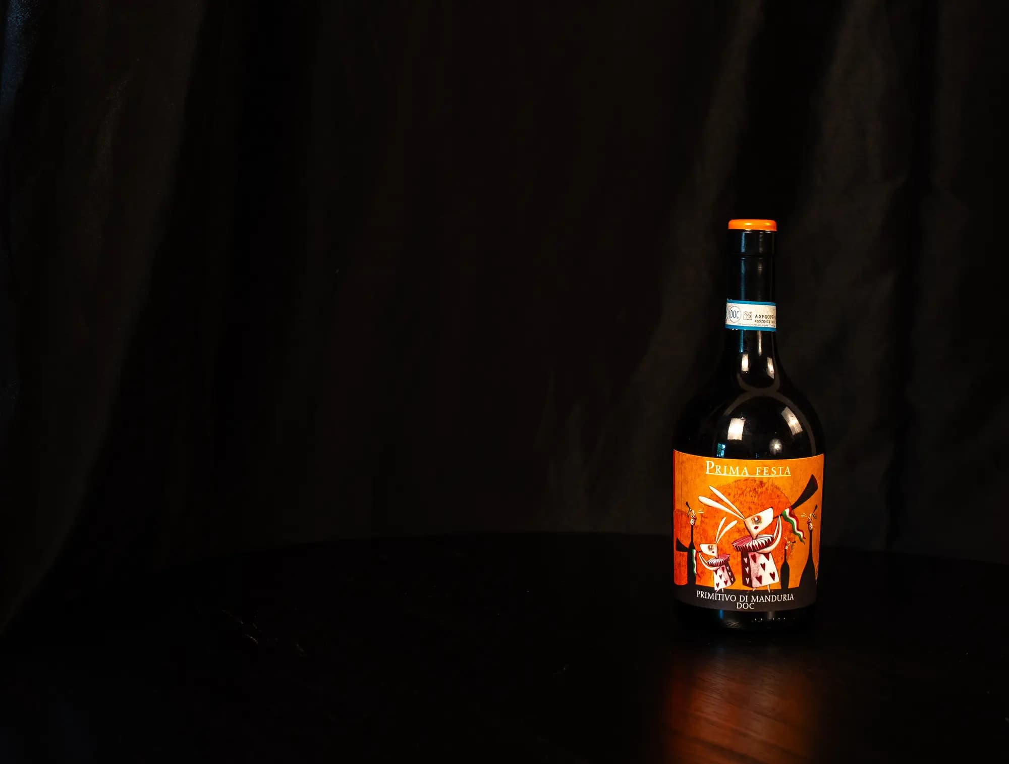 Fles Prima Festa Primitivo di Manduria met opvallend oranje etiket tegen zwarte achtergrond