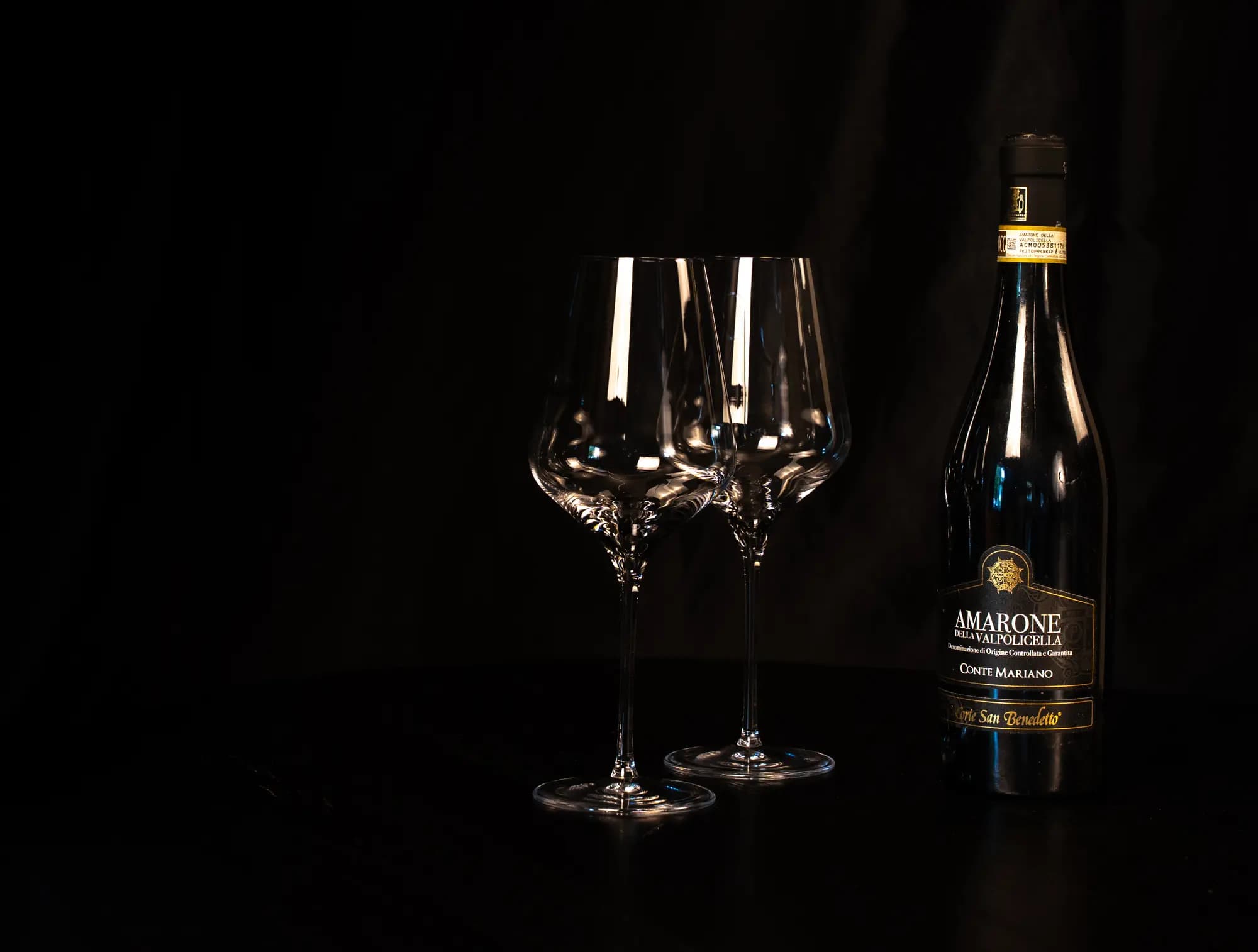 Fles Amarone della Valpolicella Conte Mariano naast twee lege wijnglazen in warm sfeerlicht